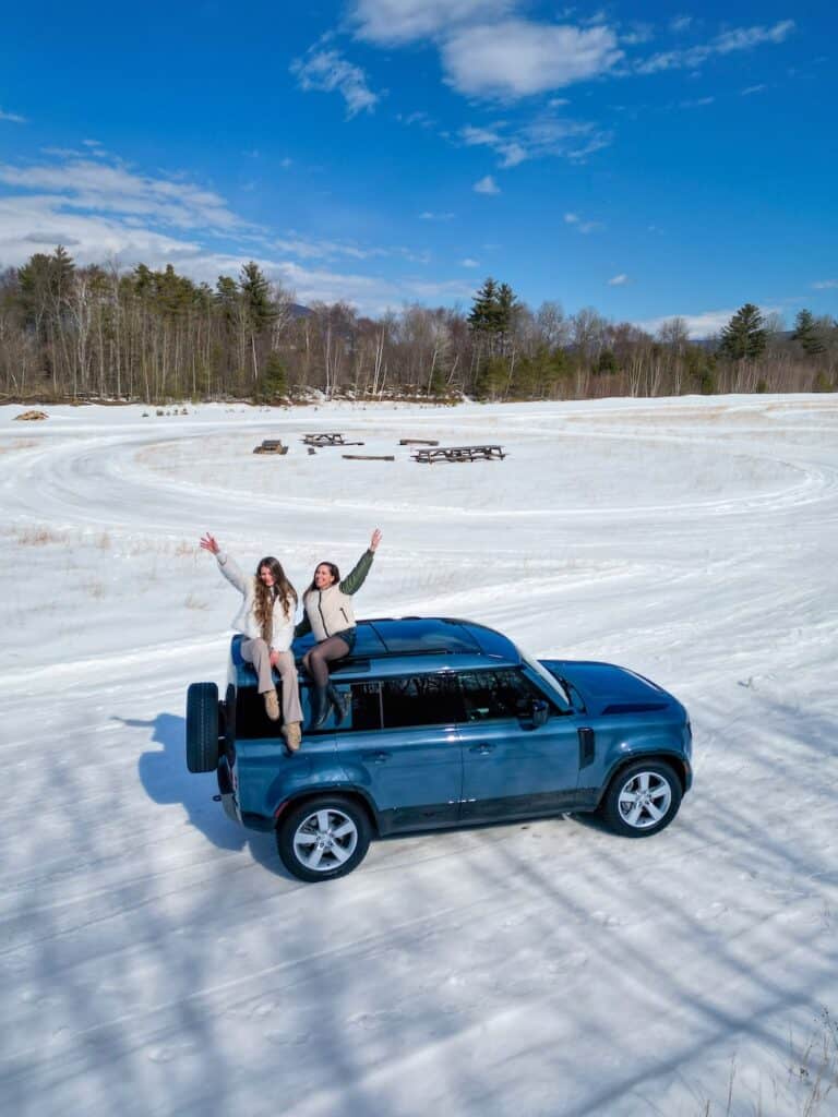 Laura and her friend sitting on a Land Rover Defender in the snow during a winter road trip in Manchester Vermont