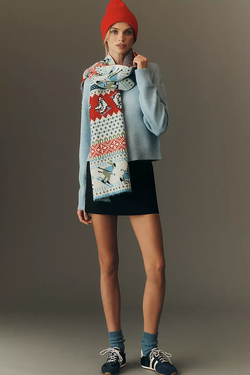 Model wearing a colorful fair isle scarf with winter motifs, styled with a light blue sweater and red beanie