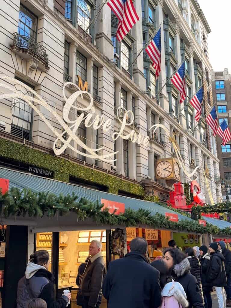 Macy’s Herald Square outdoor holiday market with festive wooden chalets and shoppers in Midtown NYC