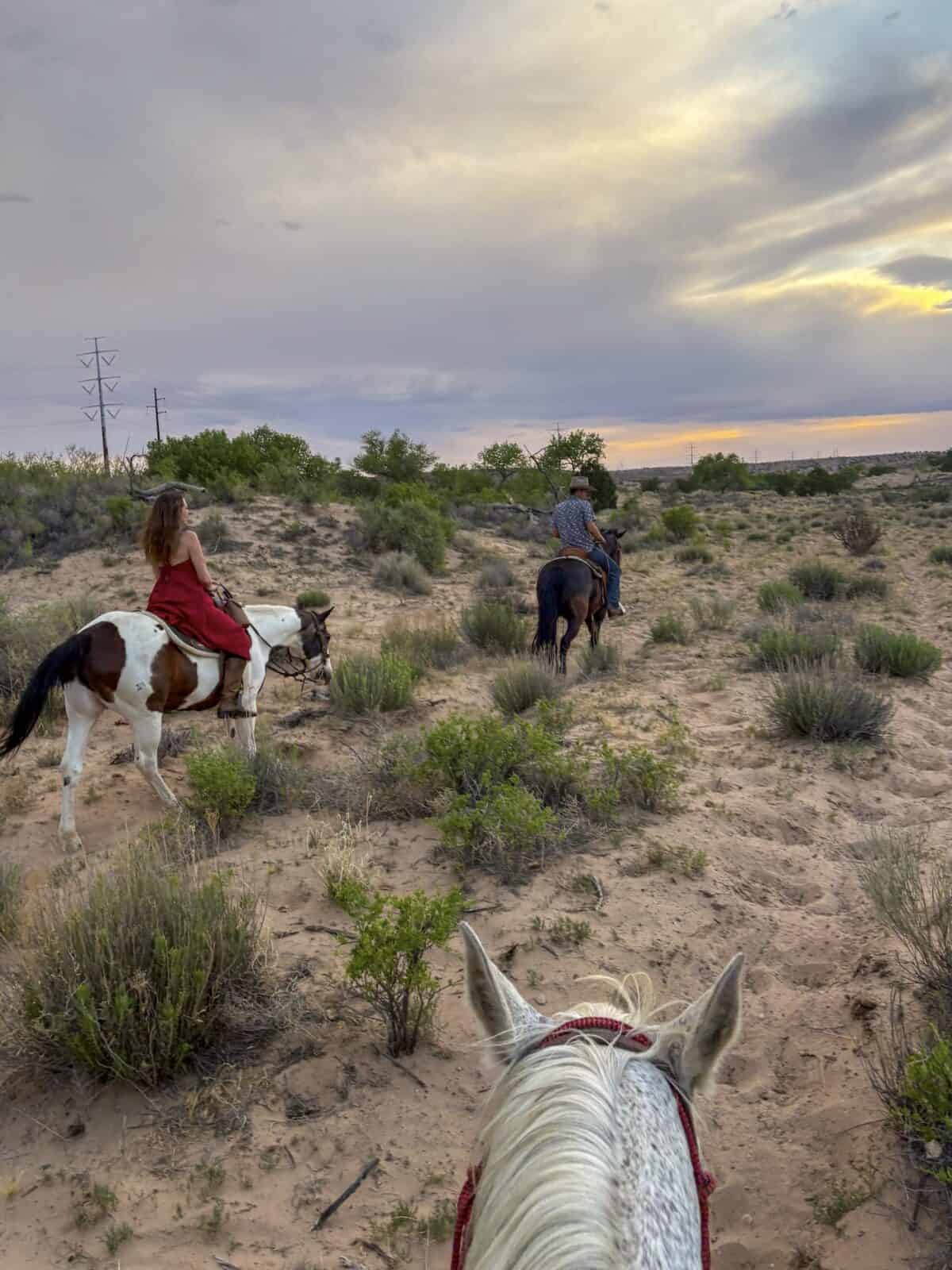 Laura in a red dress riding a paint horse through the high desert at sunset on a Tamaya Horse Rehabilitation trail ride