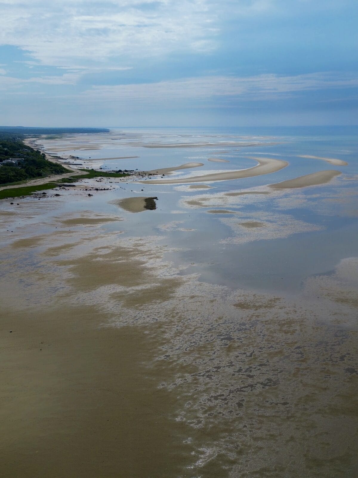 An expansive drone aerial shot looking out over the winding sandbars and shallow blue water channels of the Brewster Flats at low tide, showcasing the vast patterns carved into the coast.