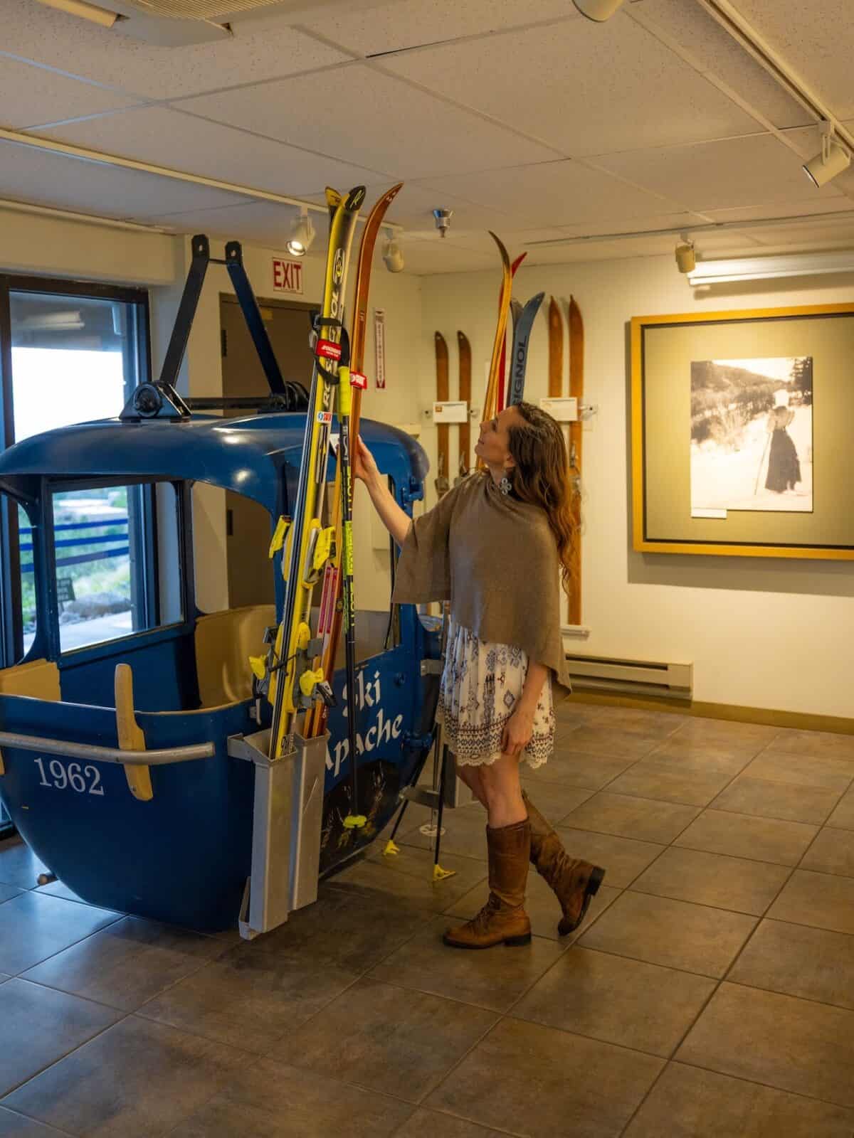 Laura looking at vintage skis beside the historic 1962 gondola at the Ski Hall of Fame on Sandia Peak, Albuquerque