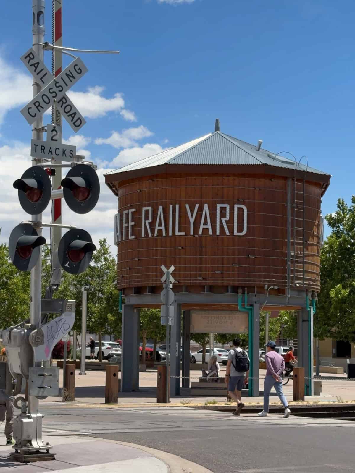 The historic wooden water tower marking the Santa Fe Railyard district beside a railroad crossing sign under a blue sky